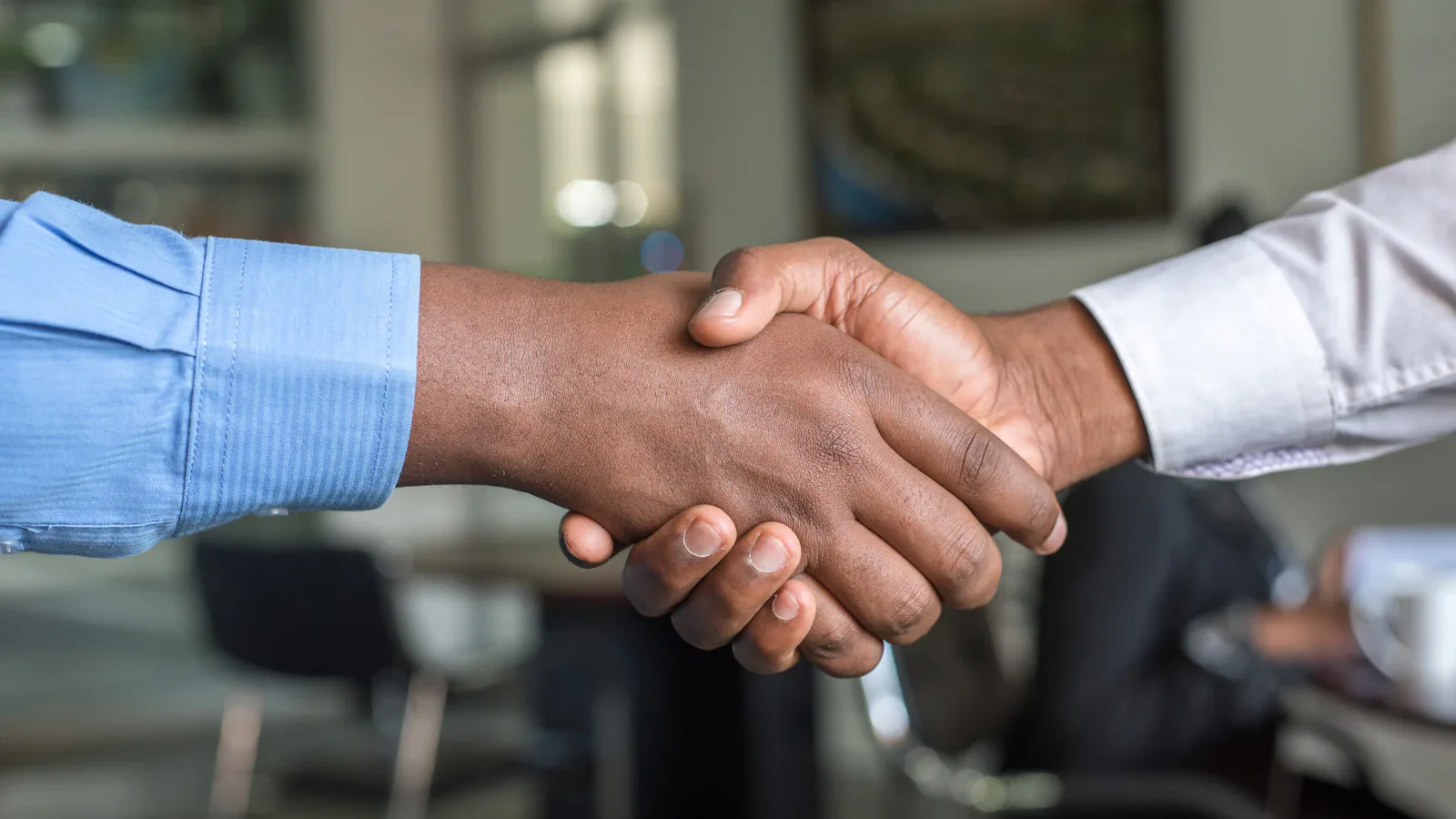 Two people shaking hands across a desk, the moment a founder commits to a new hire
